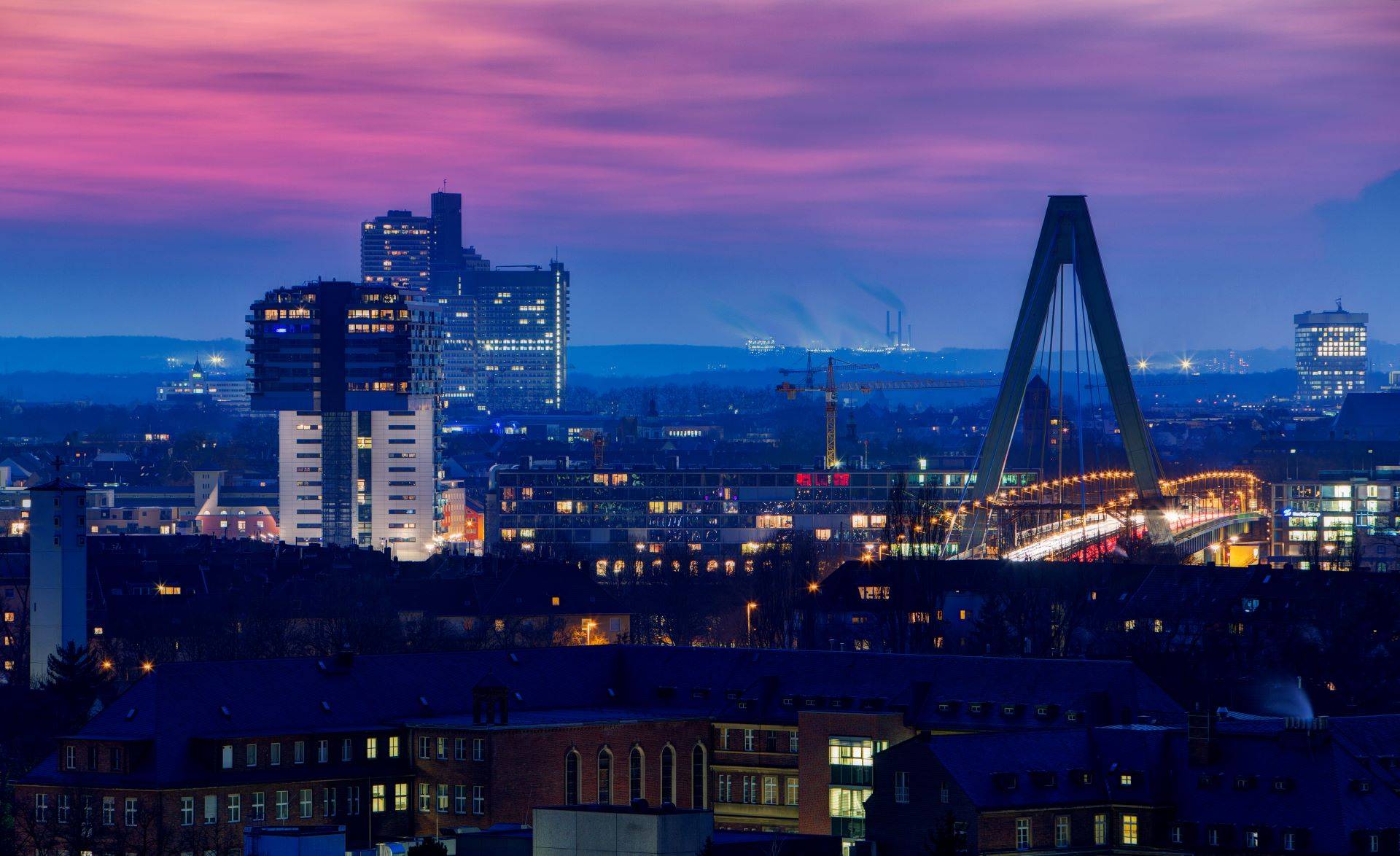 Kölner Skyline bei Nacht mit beleuchteter Brücke.