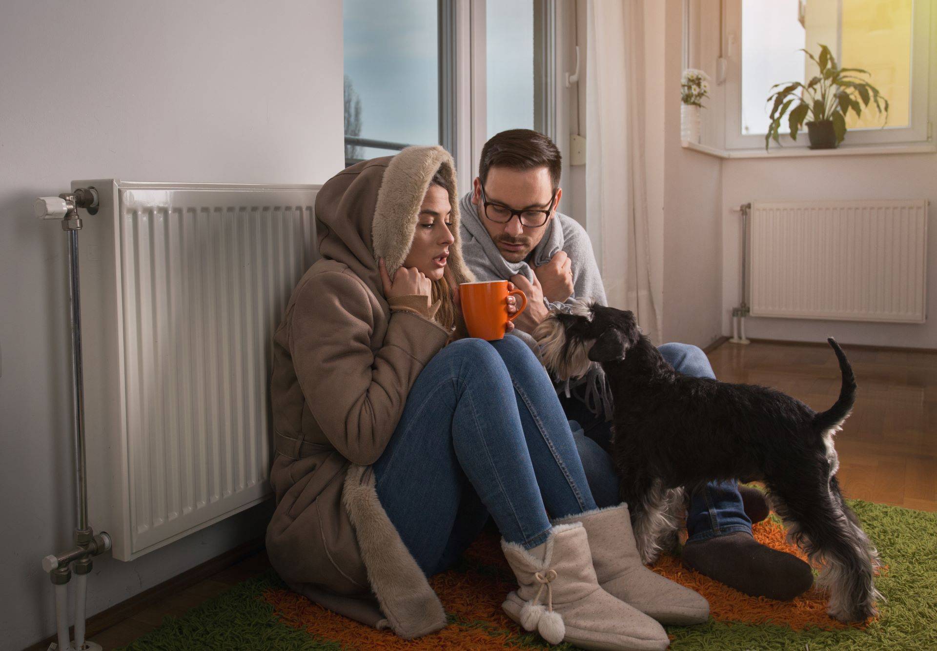 Paar sitzt in Winterkleidung vor kaltem Heizkörper