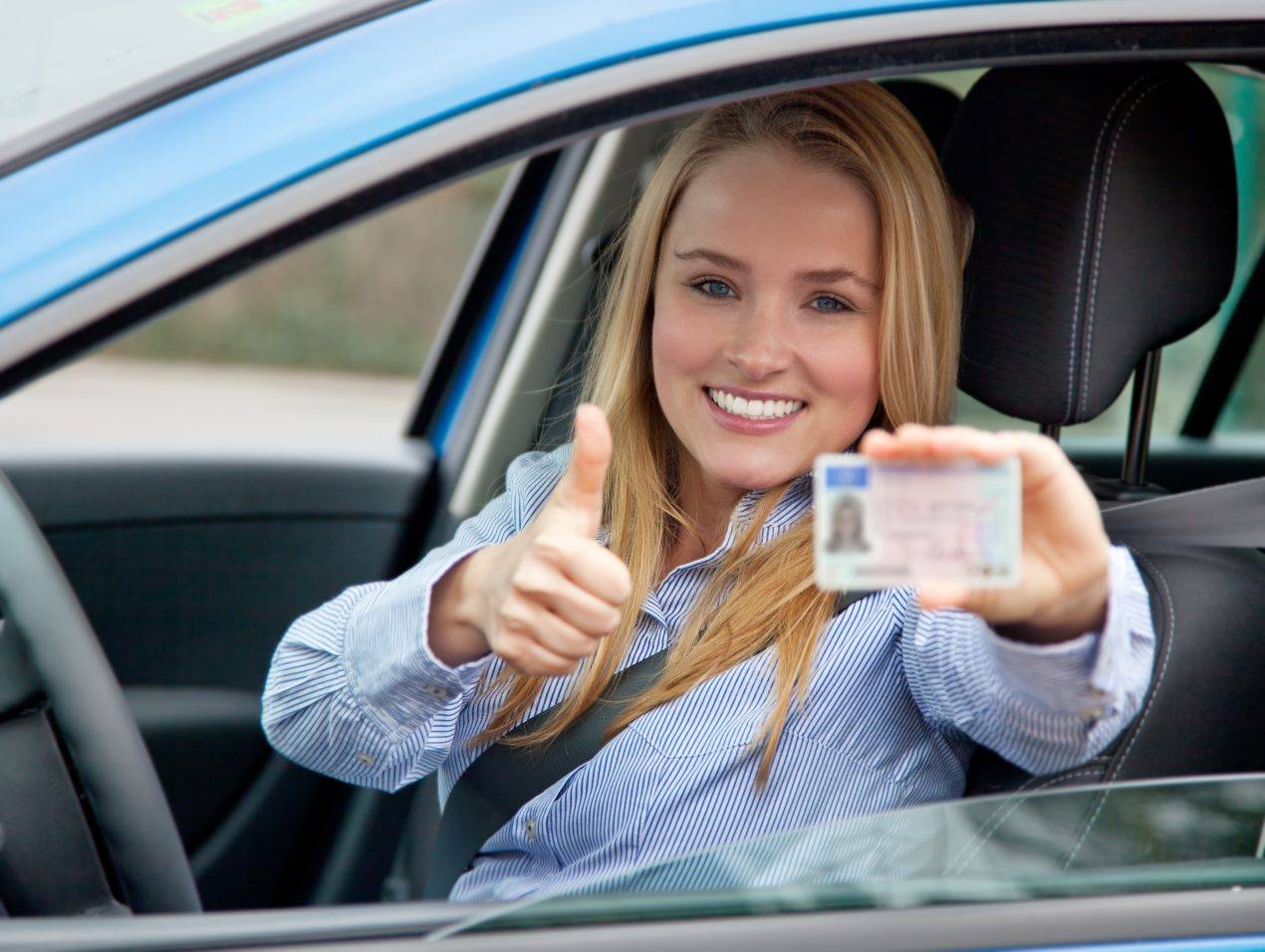 Junge Frau im Auto zeigt lächelnd ihren neuen Führerschein nach dem Fahrtraining in Zürich.