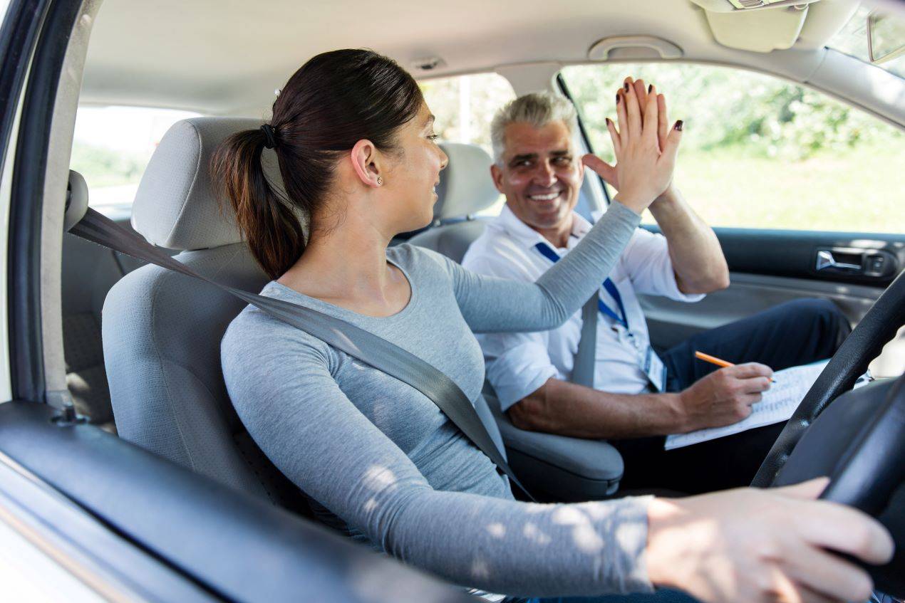 Junge Fahrerin gibt ihrem Fahrlehrer ein High-Five nach einer erfolgreichen Fahrstunde.