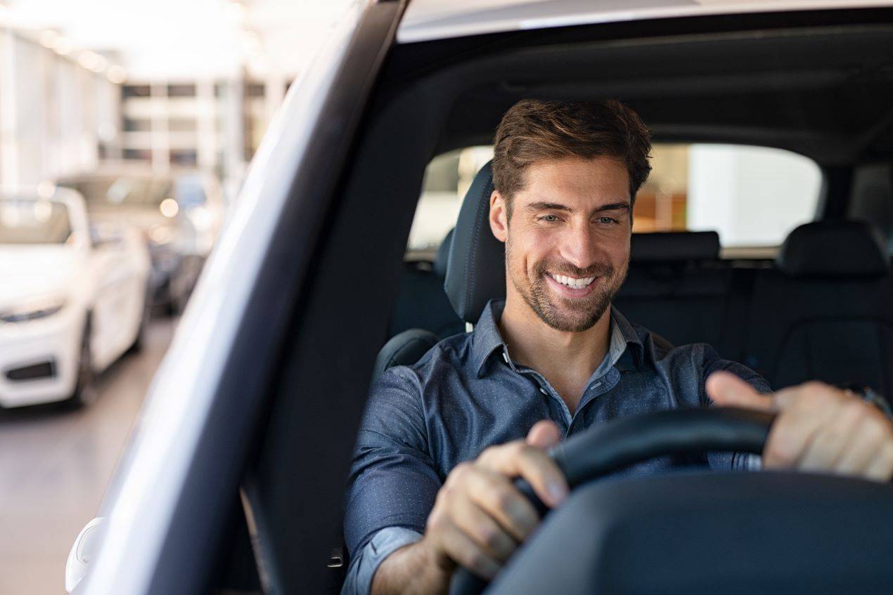 Lächelnder Mann hinter dem Steuer eines Autos bei der Probefahrt im Autohaus