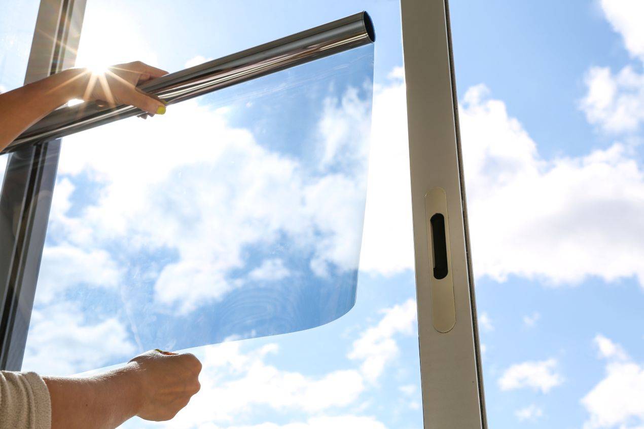 Eine Person bringt eine transparente Fensterfolie blickdicht an einem Fenster an, während Sonnenlicht durchscheint.